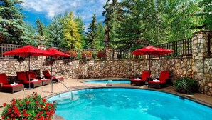 A pool area with red umbrellas, lounge chairs, and a stone wall. - Luxury 3-Bedroom Penthouse-style Retreat in Beaver Creek Village (Beaver Creek)