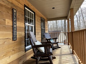 A wooden cabin with a porch, two rocking chairs, and a 'WELCOME' sign.