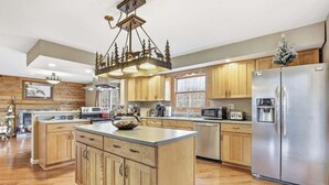 A spacious kitchen with wooden cabinets, a central island, stainless steel appliances, and a decorative chandelier. - Cabin. Hocking county ,private , secluded. Family, Friends. (Rockbridge)