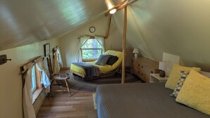 Een gezellig zolderkamer met een bed, een tafeltje en een raam met gordijnen.