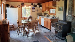 Een keuken met houten kastjes, een stenen openhaard en een eethoek met een ronde tafel en stoelen.
