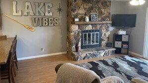 Ein Wohnzimmer mit Kamin aus Stein, einem an der Wand befestigten Fernseher und einem Essbereich mit Holztisch und Stühlen.
