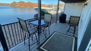 Eine überdachte Terrasse mit Tisch und Stühlen, mit Blick auf einen See mit Booten und Stegen.