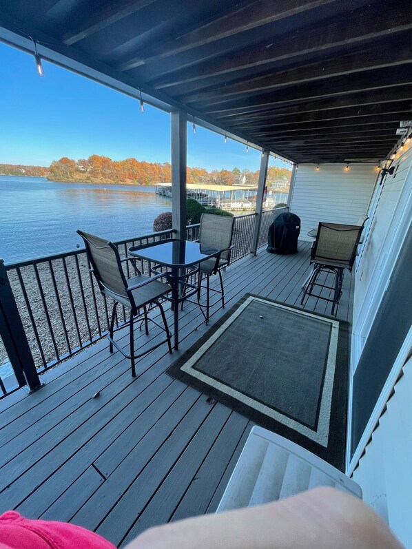 A covered deck with a table and chairs, overlooking a lake with boats and docks.