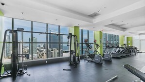 Ett modernt gym med stora fönster, träningsutrustning och utsikt över staden.