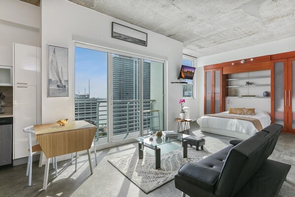 A modern hotel room with a balcony, a bed, a desk, and a TV.