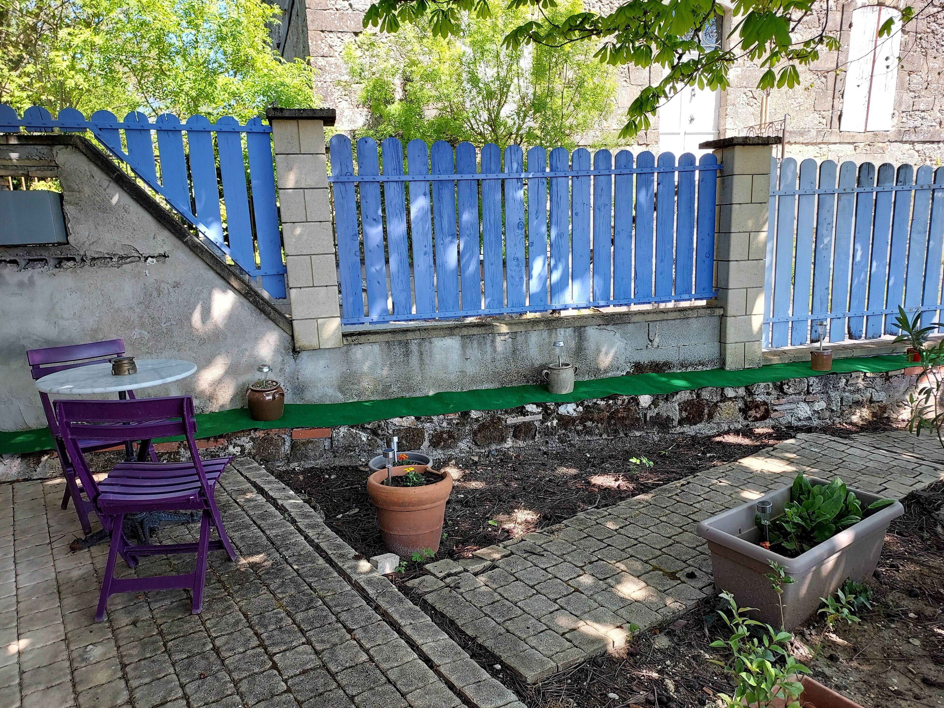 A patio with a purple chair, a small table, and a blue fence.