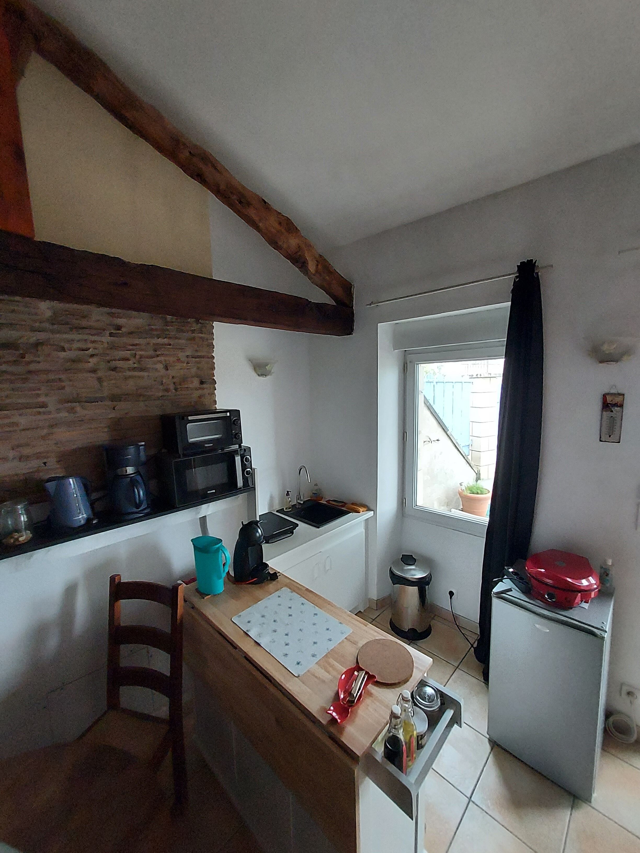 A compact kitchen with a wooden beam ceiling, a small sink, and a window with a curtain.