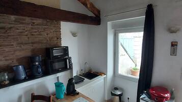 A compact kitchen with a wooden beam ceiling, a small sink, and a window with a curtain.