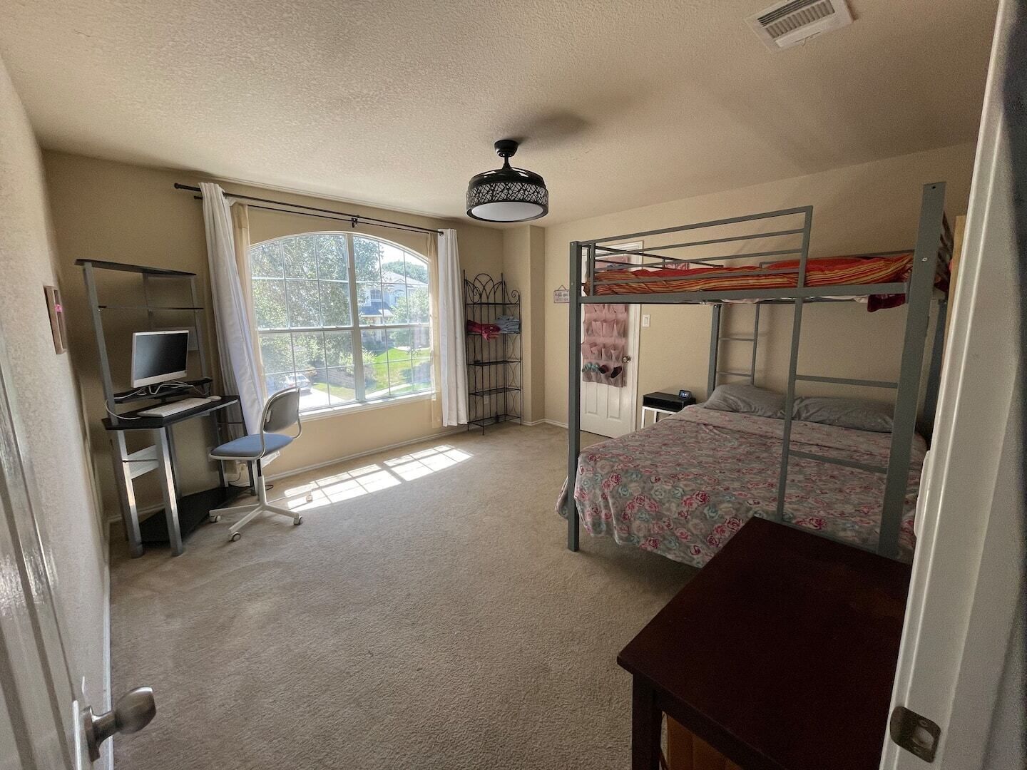 Ein Schlafzimmer mit Etagenbetten, einem Schreibtisch mit Computer, einem Stuhl und einem Bett mit Blumenmuster-Bettwäsche.