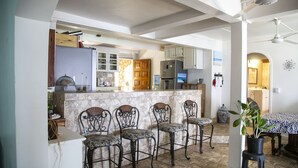 Une cuisine dotée d’un îlot central en pierre, de quatre tabourets de bar et d’un coin repas avec une table et des chaises.