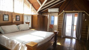 Une chambre à coucher en bois, dotée d’un grand lit, d’un plafond en bois et d’une porte-fenêtre coulissante donnant sur un espace extérieur.