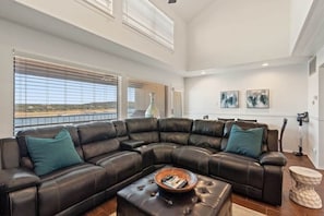 A modern living room with a large L-shaped leather sofa, a coffee table, and artwork on the walls. - Lakefront Family Escape|Boat Slip · Pool · Hot Tub (Spicewood)