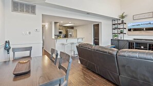 Ein modernes Wohnzimmer mit einer Ledersofa, einem Esstisch mit Stühlen, einer Küche im Hintergrund und einem Deckenventilator.
