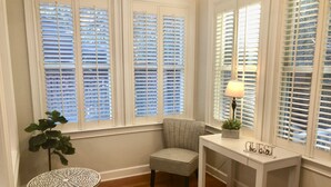 Una habitación acogedora con un sillón gris, una mesita redonda y un escritorio con lámpara.