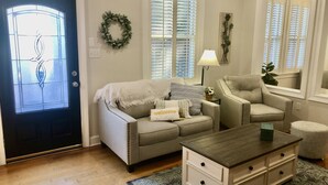Una sala de estar con sofá, sillón, mesa de centro y puerta decorada con un adorno festivo.