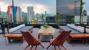 Una terraza en la azotea con mobiliario de madera, una mesa de madera en el centro y vistas a un horizonte urbano.