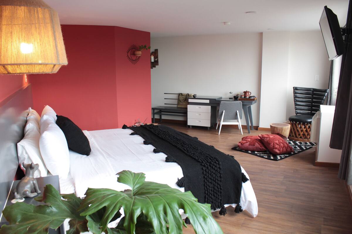 A bedroom with a bed, desk, chair, and a plant.