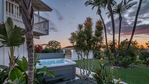 A modern house with a hot tub, a balcony, and a well-maintained garden with palm trees and tropical plants.