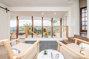 A spacious balcony with a view of mountains and a pool, furnished with wooden chairs and a marble table. - Stunning Views w/ Game Room, Pool and Hot Tub! (Escondido)