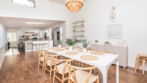 A spacious dining area with a long white table, wooden chairs, and woven placemats.