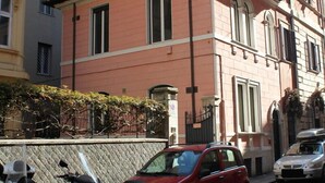 Une voiture rouge est garée sur une rue pavée, avec un scooter et une moto à proximité.