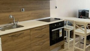 A modern kitchen with wooden cabinets, a built-in oven, a sink, and a dining area with a white table and chairs. - Vanessa room (Orlando)