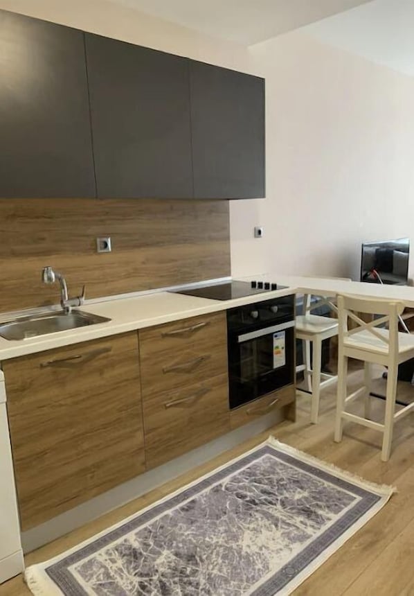 Una cocina moderna con armarios de madera, horno empotrado, un lavamanos y una zona de comedor con mesa y sillas blancas.