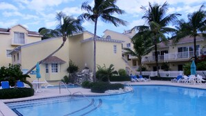 A swimming pool with lounge chairs and palm trees, surrounded by buildings with balconies. - Sunrise Beach Villas #2.. Oceanfront Villa (New Providence)