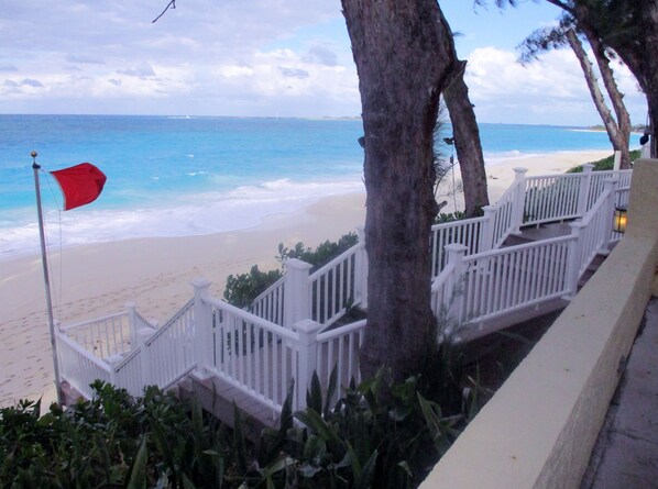 Una escalera que lleva a una playa con una bandera roja, barandillas blancas y palmeras.