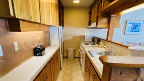 A narrow kitchen with wooden cabinets, a white countertop, a sink, and a trash can. - Available 1 week only: 
 Prime ski week Feb 22 - March 1 Sunday - Sunday (Wilson)