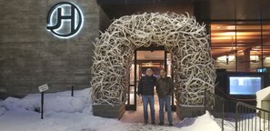 A hotel entrance with a large, illuminated logo, a sign indicating a connection to a nearby location, and a unique antler archway.