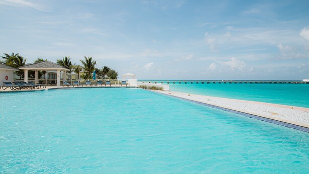 A clear blue pool with a white deck, palm trees, and a distant pier. - "Footprints in the Sand" - Poolside 3/3 (Bailey Town)