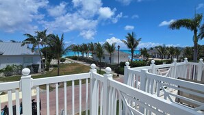 A coastal hotel with white railings, palm trees, and a clear view of the ocean. - "Footprints in the Sand" - Poolside 3/3 (Bailey Town)