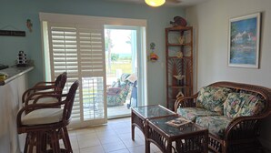 A living room with a wicker sofa, a glass coffee table, and wicker chairs. There is a sliding glass door leading to a patio area. - "Footprints in the Sand" - Poolside 3/3 (Bailey Town)