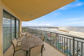 Un balcón con mesa y sillas, con vista a una playa y un puerto deportivo.