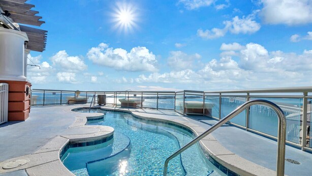 A pool area with a clear view of the sea, a sunshade structure, and a lifeguard stand. - Emerald Grande ❤️❤️ 7th Floor Corner Unit 😎😎 Wrap Around Balcony 🐠🐠 EV Chargers 🦀🦀 (Destin)