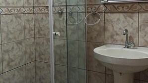A bathroom with a glass shower enclosure, a sink, and tiled walls. - Arraial do Cabo - Apartment 04 - Brisas do Farol - Affordable Rental (Arraial do Cabo)