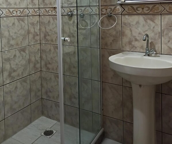 Une salle de bain avec une douche à parois de verre, un lavabo et des murs carrelés.
