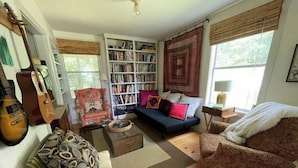 A cozy living room with a bookshelf, a sofa, a chair, and a guitar.