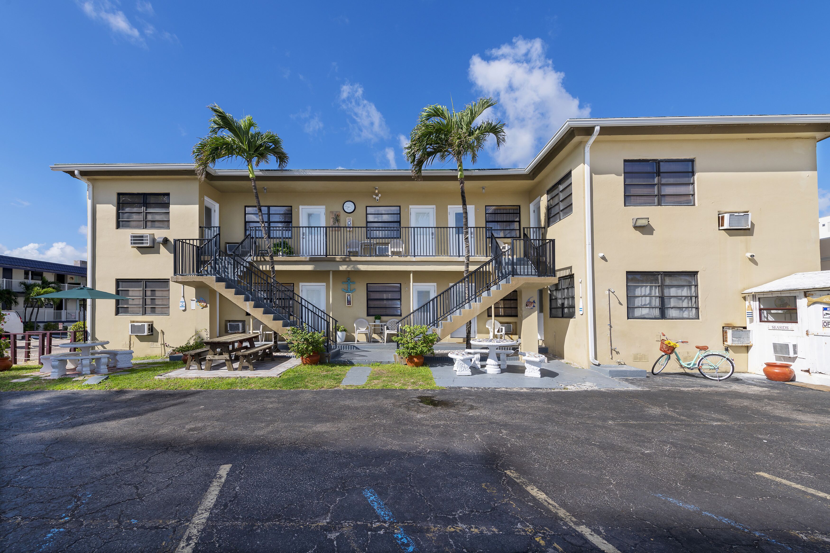 A two-story building with a balcony, palm trees, and a bicycle parked outside.