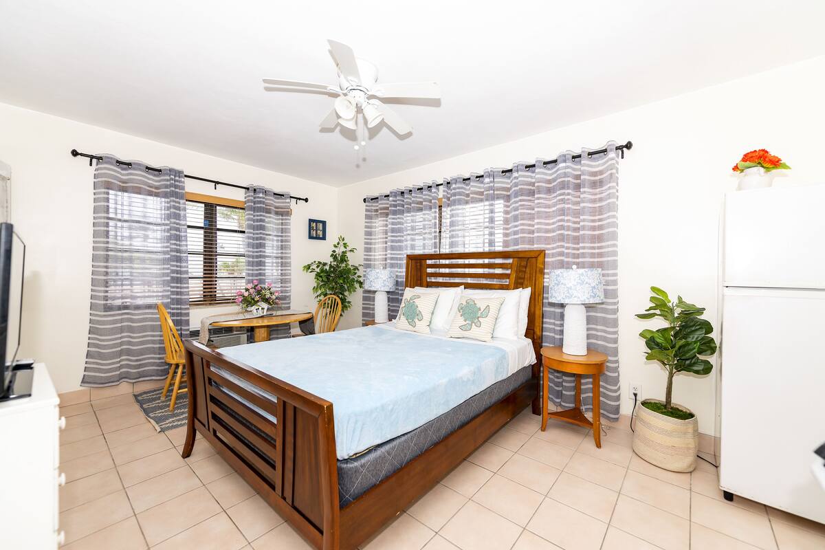 Ein Schlafzimmer mit einem Holzbett, einem Deckenventilator, einem Schreibtisch und einer Topfpflanze.