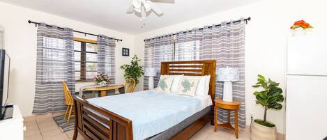 Un dormitorio con una cama de madera, un ventilador de techo, un escritorio y una planta en maceta.