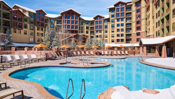 Ein Poolbereich eines Resorts mit mehreren Gebäuden, Liegestühlen und einem zentralen Pool.