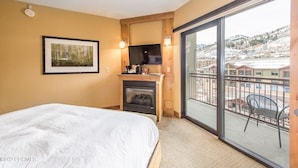 Ein Schlafzimmer mit Bett, Kamin, Fernseher und einem Balkon mit Blick auf eine verschneite Landschaft.