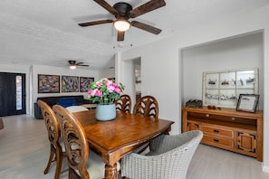 Un coin repas avec une table en bois, des chaises, un ventilateur de plafond et un vase de fleurs.