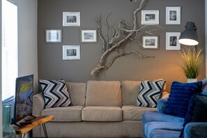 Un salon avec un canapé, une table basse, une lampe et des tableaux accrochés au mur.