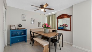 Ein Essbereich mit Holztisch, vier Stühlen, einer Bank, einem Deckenventilator, einem an der Wand befestigten Spiegel und einer blauen Konsole mit Dekorationen.