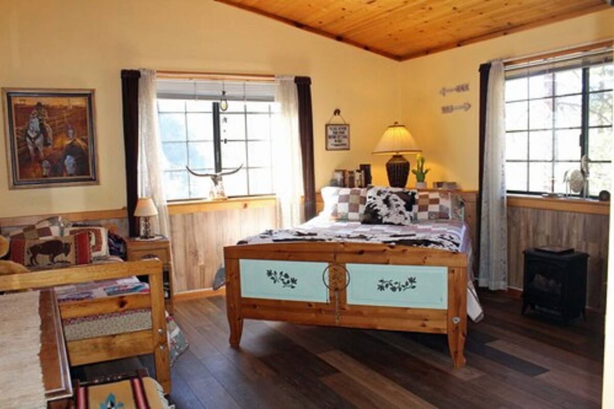 A cozy bedroom with a wooden bed, a nightstand, a lamp, and a window with curtains.