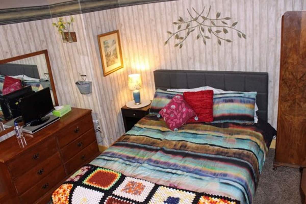 A bedroom with a bed, a dresser, a nightstand, a lamp, and a wall decoration.